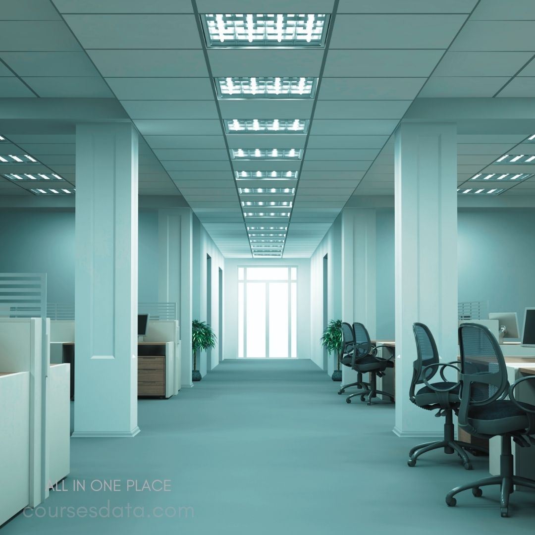 Modern office corridor view. Bright overhead lights illuminate space. Empty desks with ergonomic chairs. Green plants add subtle decoration. Large window at far end.