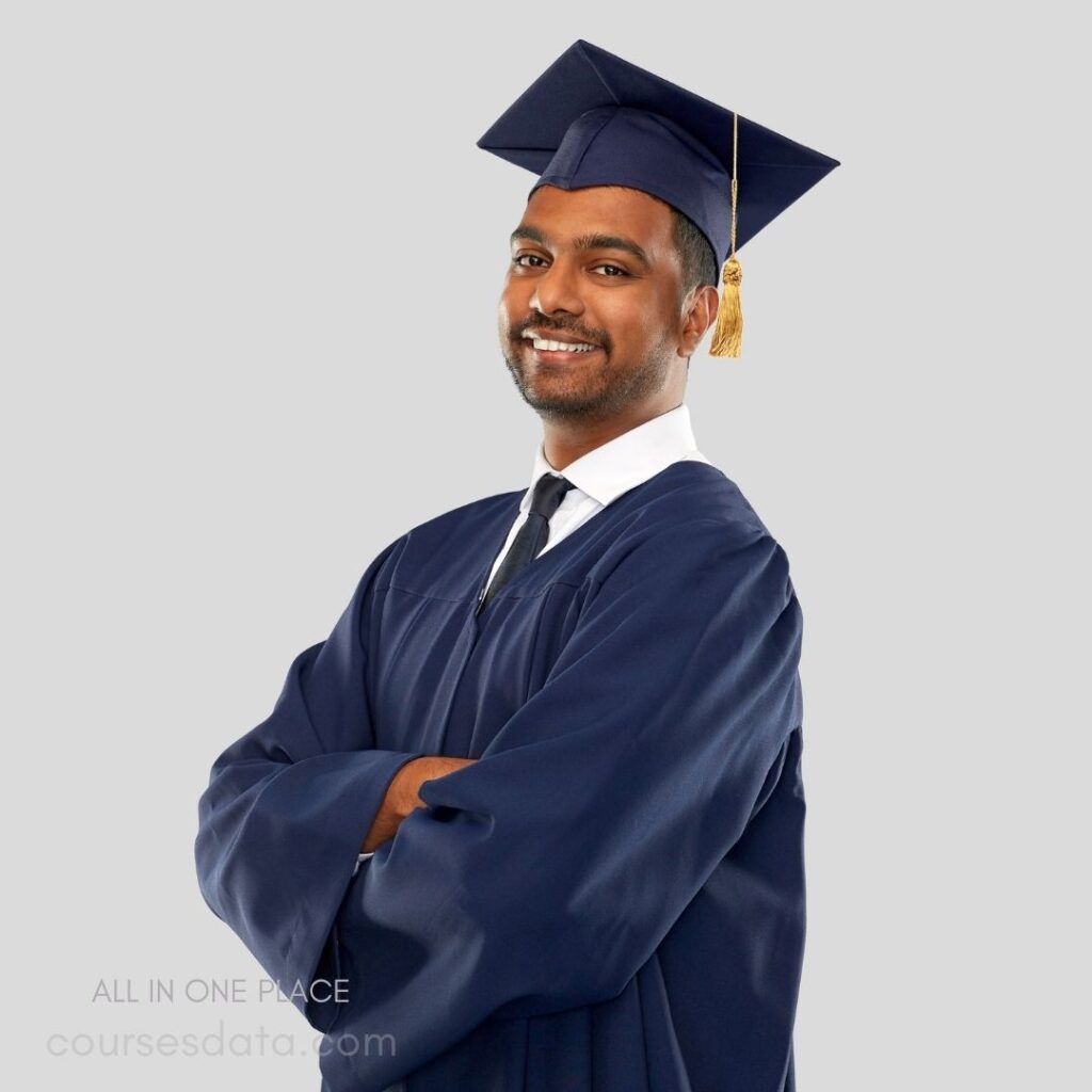 Happy graduate in cap. Navy graduation gown. Confident pose and smile. Neutral gray background. Celebratory moment captured.