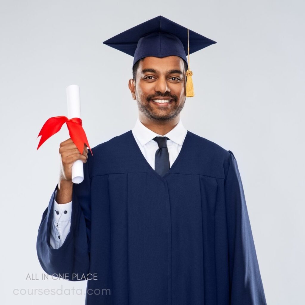 Graduating student with diploma. Wearing graduation cap and gown. Smiling against plain background. Red ribbon tied on diploma. Formal attire underneath gown.