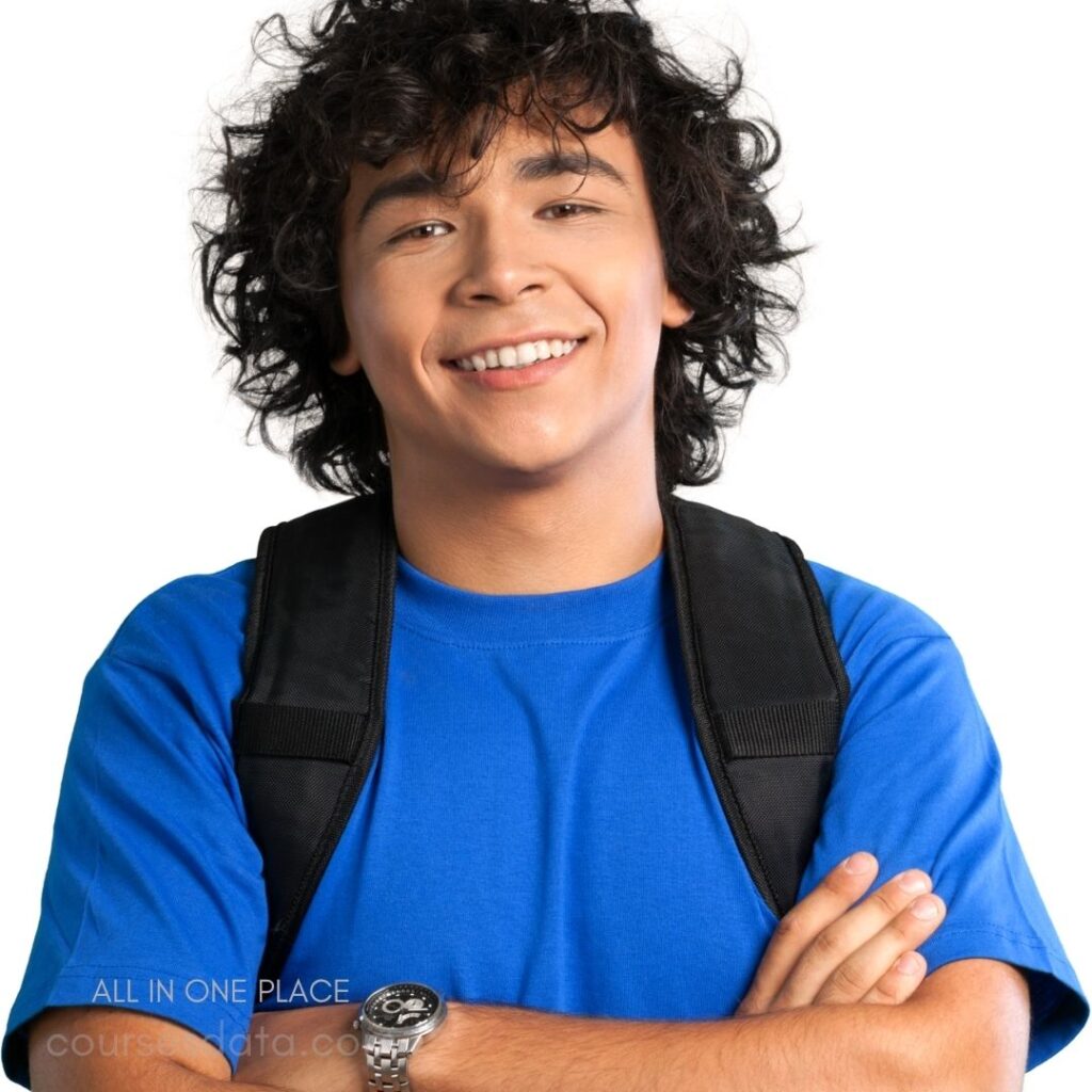 Smiling young man, curly hair. Wearing blue t-shirt, backpack. Arms crossed confidently, casual pose. White background, bright lighting. Showing friendly, approachable demeanor.